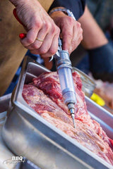 A person is slicing a piece of meat with the SpitJack Magnum Meat Injector Gun - Complete Kit with Deluxe Hard Case.