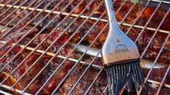 Ribs on a grill with the SpitJack Silicone & Stainless BBQ Brush Set.