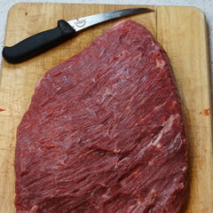 A piece of steak on a cutting board with the SpitJack Meat Trimming and Boning Knife - 6 Inch Curved Blade.