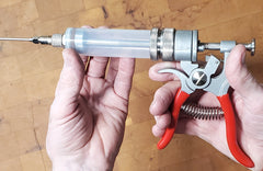 A hand is holding a SpitJack Magnum Meat Injector Gun - Complete Kit with Padded Soft Case with a red and white nozzle.