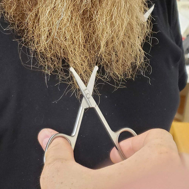 A person holding SpitJack Utility Mini Scissors (4 Inch Stainless Steel) from a 2 Pack is about to cut the ends of a long, blonde beard.