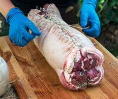 A person is preparing a large piece of meat on a SpitJack Butcher's Twine 3 Pack (555-Feet) cutting board.