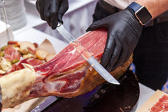 A person cutting a Deluxe Brisket Slicing Knife - 11 Inch Blade, Competition-Chef Series ham in black gloves from SpitJack.