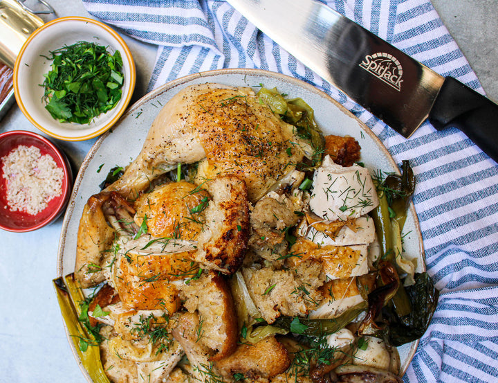 A plate of chicken and vegetables on a table next to a SpitJack 8 inch Chef Knife and Sharpening Hone Combo. Professional Chopping and Cooking Kitchen Knife Set.