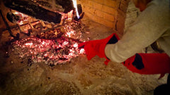 A person wearing SpitJack Deluxe Fireplace - Barbecue Gloves FP gloves is holding a fire in a fireplace.
