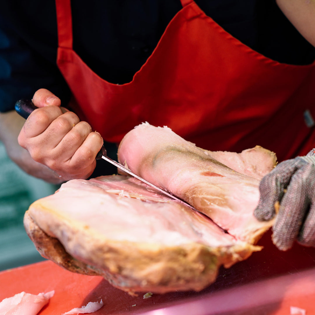 A person using a SpitJack Deluxe 11" Slicing Knife and 6" Boning Knife Bundle to cut a piece of meat.