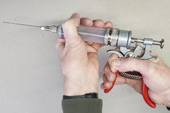 A man is holding the SpitJack Magnum Meat Injector Gun - Complete Kit with Padded Soft Case.