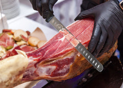 A person cutting a piece of meat with a SpitJack Brisket, Ham, Turkey Carving and Carving Knife - 11 inch blade.