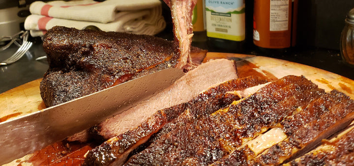 A person cutting a piece of ribs on a SpitJack 6 Inch Beef Brisket Trimming and Boning Knife and 11" Slicing Knife Bundle. Stainless Steel cutting board.