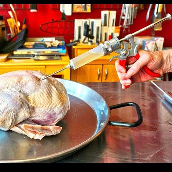 A hand uses the SpitJack MAGNUM Meat Injector Kit with deluxe case and four needles to inject liquid into a raw turkey in a metal pan, a BBQ pros’ method for juicier, more flavorful results.