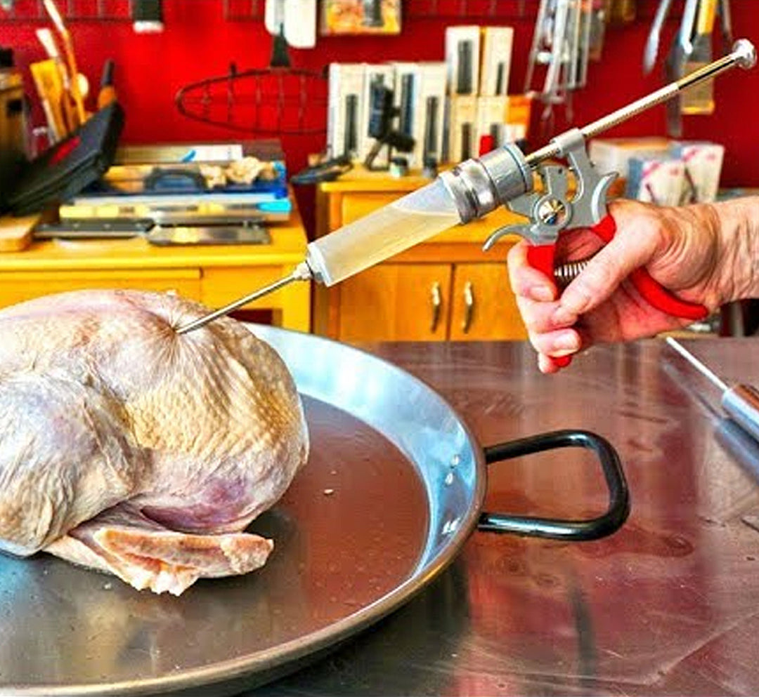 In a kitchen, someone uses the SpitJack Magnum Meat Injector with Deluxe Case and Two Needles to inject marinade into a raw turkey.